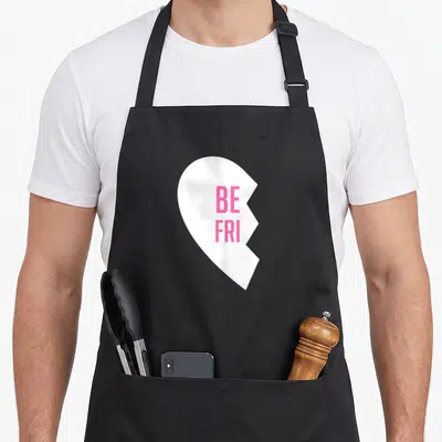 Friend chef outfit apron - Pink BE FRI text on a white heart missing its right side — shown on a black cotton canvas apron against a white background