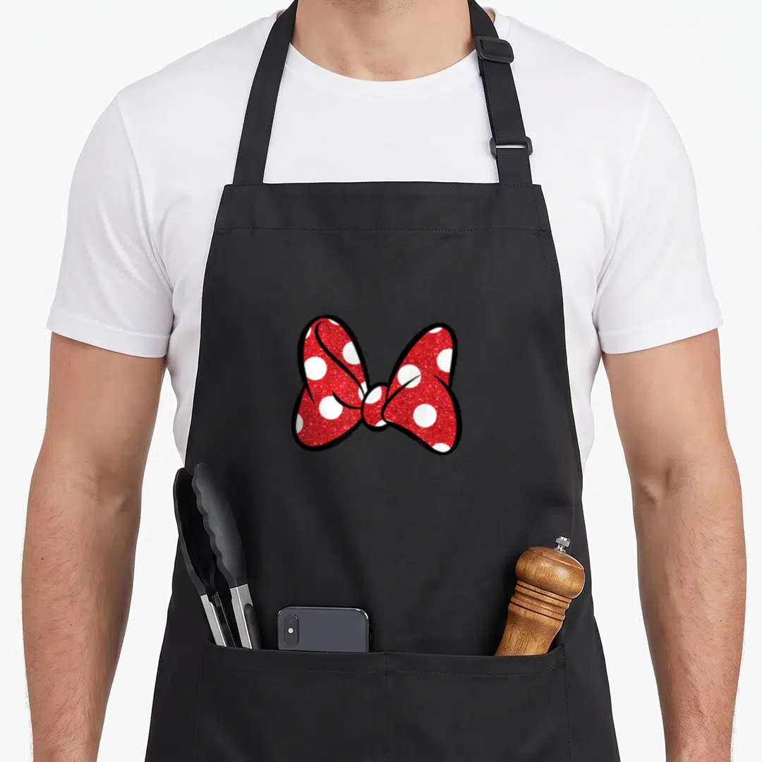 Funny bow apron - Red glittery bow with white polka dots and thick black cartoon outline — shown on a black cotton canvas apron against a white background