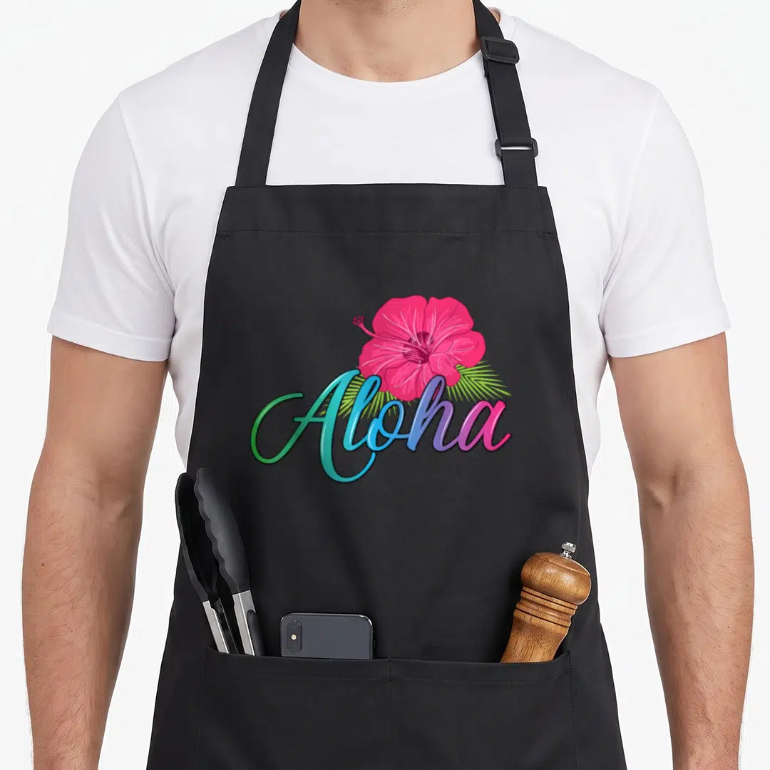 Aloha hawaii apron - Pink hibiscus flower over green palm leaf and gradient Aloha script text — shown on a black cotton canvas apron against a white background