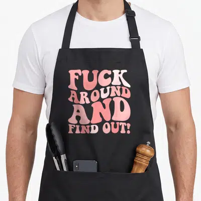 Cool around find aprons - Pink stacked typography reading FUCK AROUND AND FIND OUT! in four lines — shown on a black cotton canvas apron against a white background