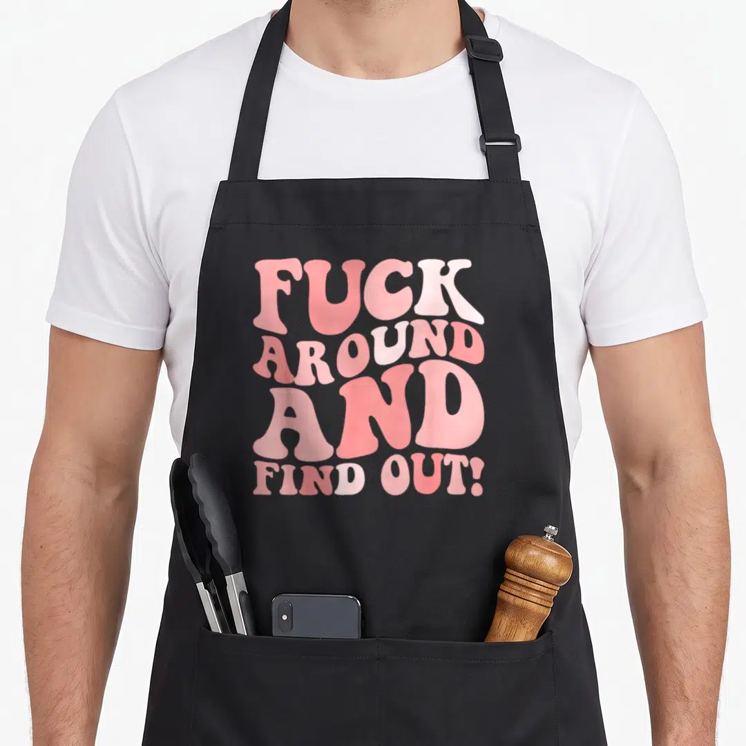 Cool around find aprons - Pink stacked typography reading FUCK AROUND AND FIND OUT! in four lines — shown on a black cotton canvas apron against a white background