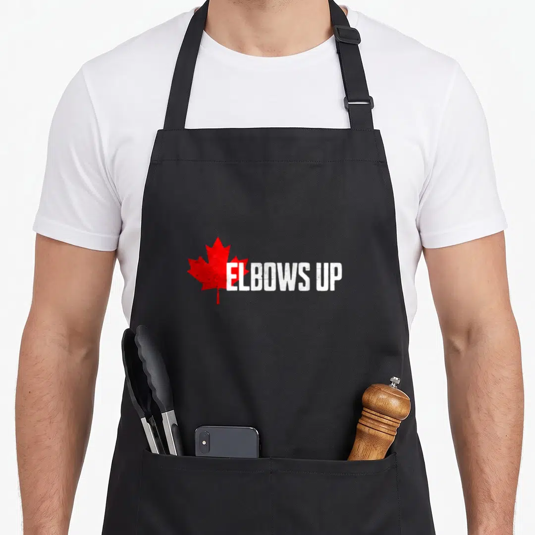Elbow canada aprons - Red maple leaf and white distressed ELBOWS UP text on black fabric — shown on a black cotton canvas apron against a white background