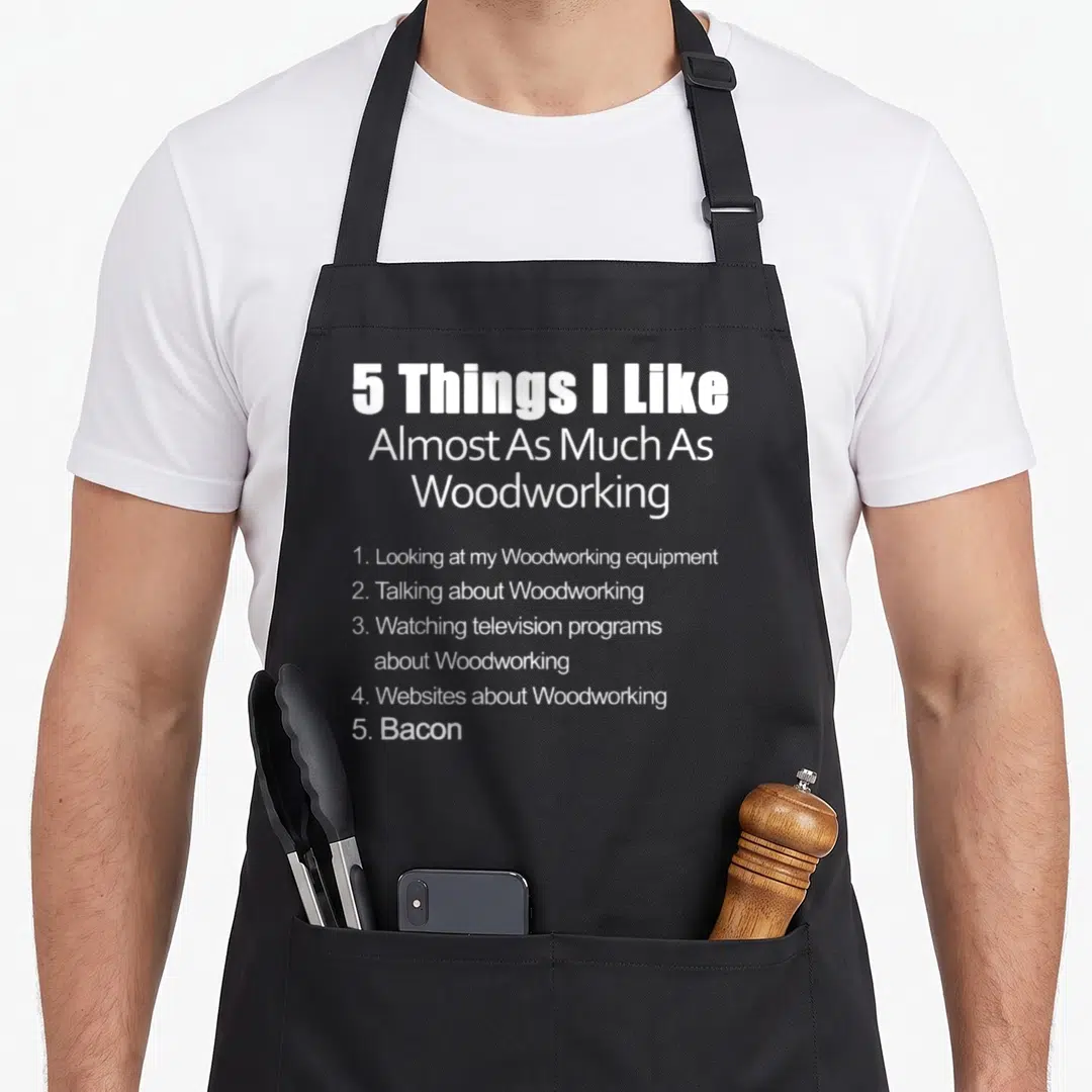 Almost woodworking apron - White text listing woodworking interests ending with bacon on gray background — shown on a black cotton canvas apron against a white background