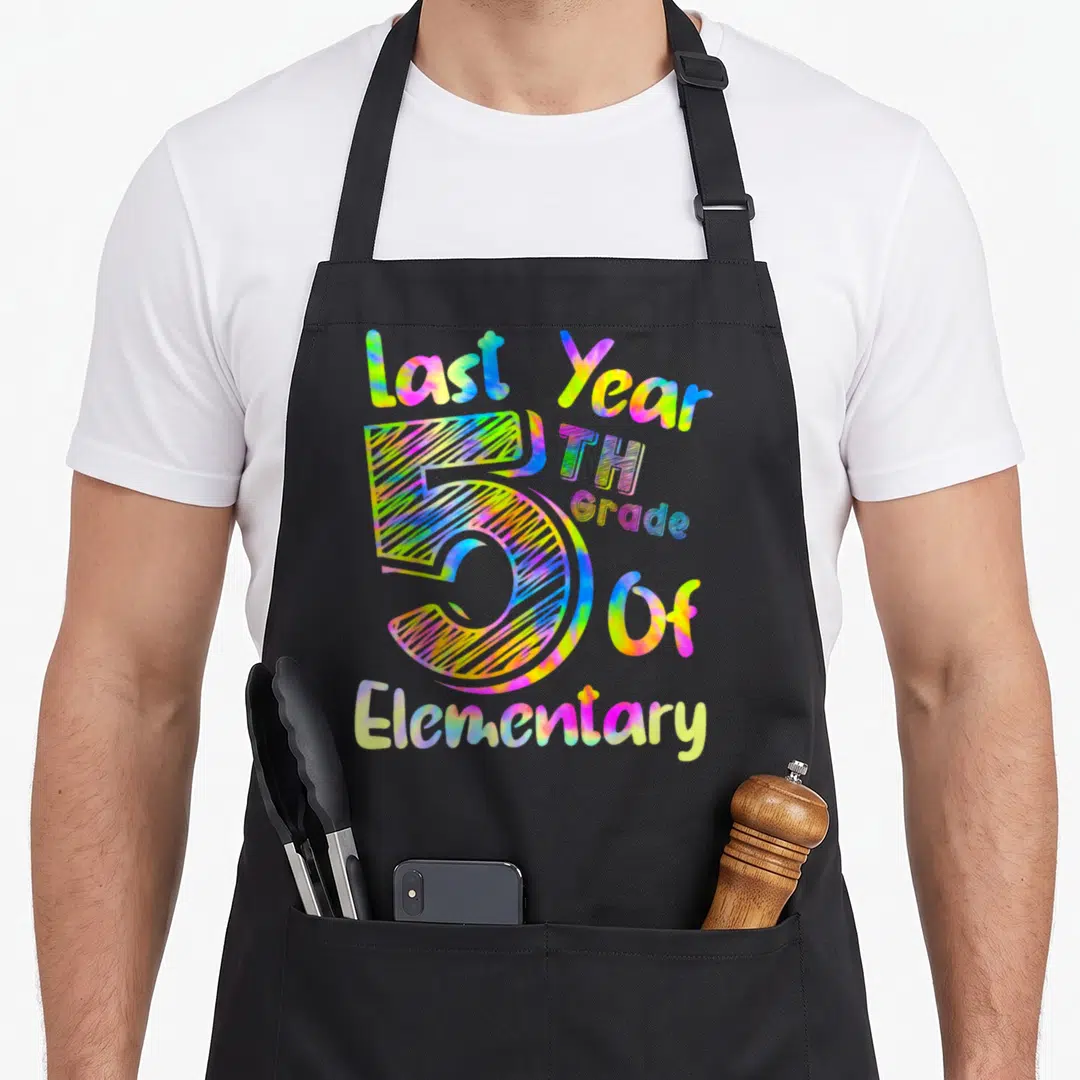 5th hello apron - Tie-dye typography reading Last Year 5TH Grade Of Elementary with large central number 5 in pink — shown on a black cotton canvas apron against a white background