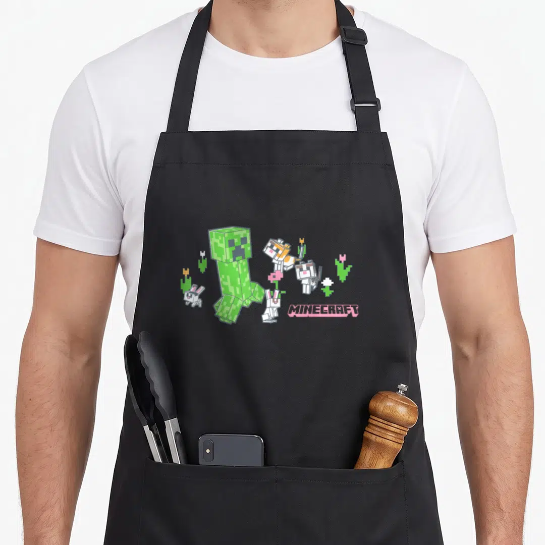 Creeper cat apron - Green pixel creeper with bunnies, cats, and pink MINECRAFT text — shown on a black cotton canvas apron against a white background