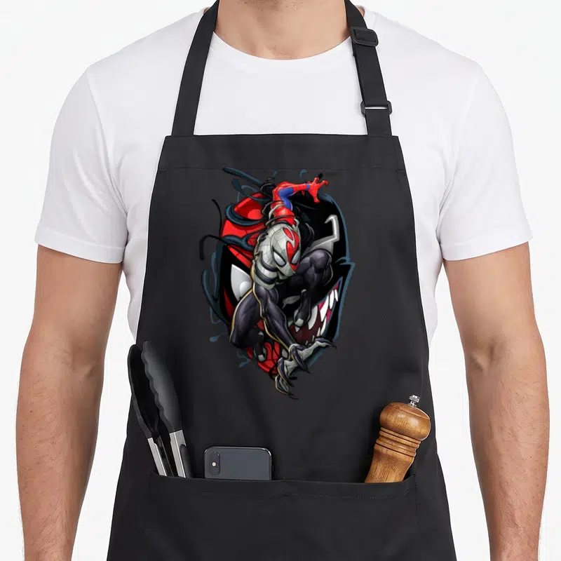 Maximum comics apron - Anti-Venom cartoon figure overlapping Venom face with Spider-Man perched on top in white black — shown on a black cotton canvas apron against a white background