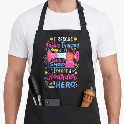 Quilting quilt apron - Pink sewing machine with I RESCUE fabric Trapped in the QUILT SHOP text and scattered tools — shown on a black cotton canvas apron against a white background
