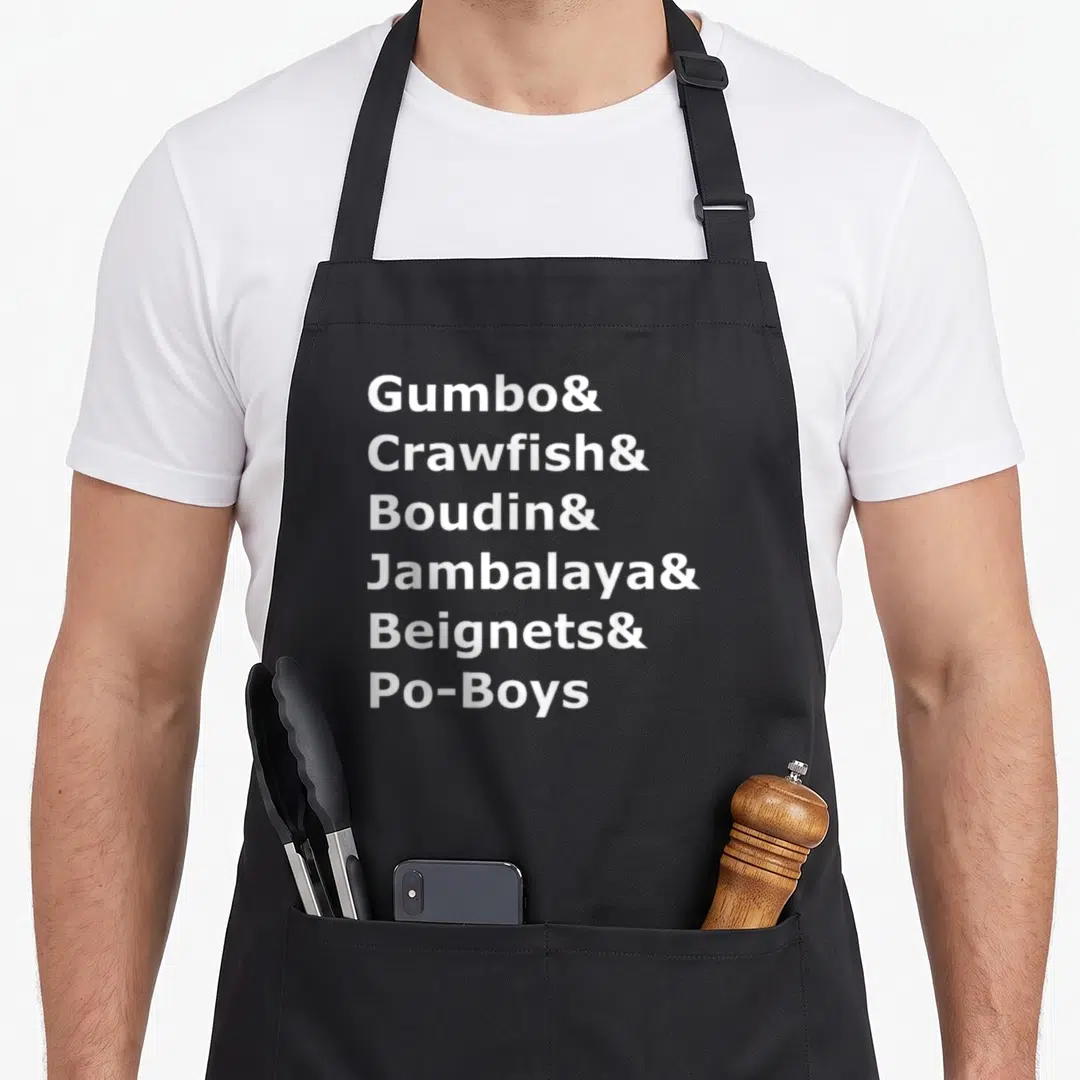 Gumbo louisiana apron - White stacked text listing Gumbo Crawfish Boudin Jambalaya Beignets Po-Boys — shown on a black cotton canvas apron against a white background