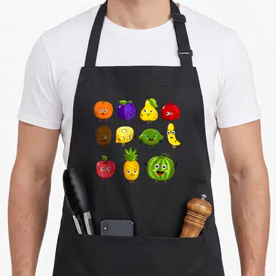 Fruit vegetable apron - Eleven cartoon fruits in three rows with orange, purple, yellow, red, brown, and green colors — shown on a black cotton canvas apron against a white background