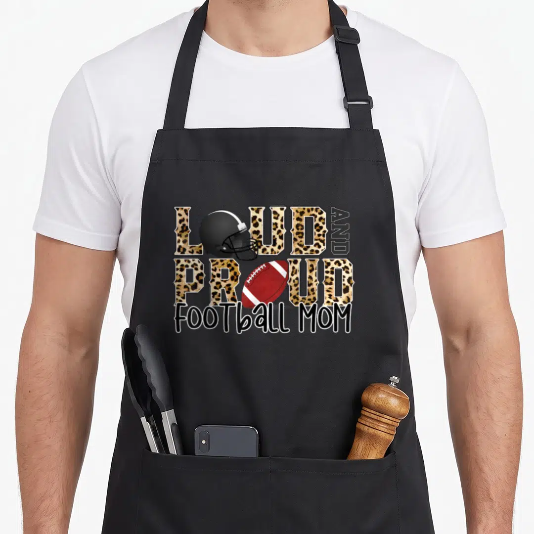 Loud leopard print cooking apron - LOUD AND PROUD FOOTBALL MOM text with helmet and football in leopard print style — shown on a black cotton canvas apron against a white background