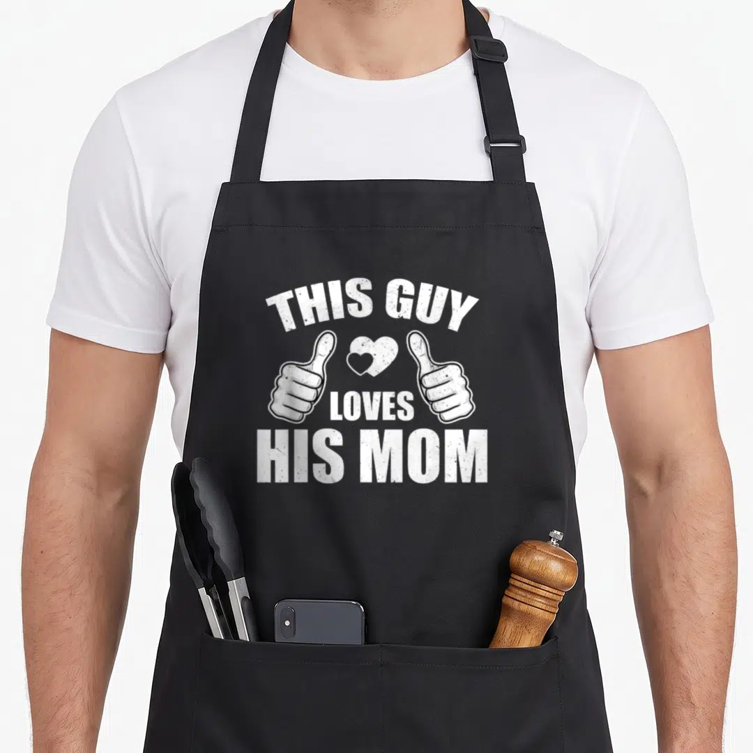 His mom and son aprons - Two white thumbs up hands with a heart between them and arched text reading THIS GUY LOVES — shown on a black cotton canvas apron against a white background