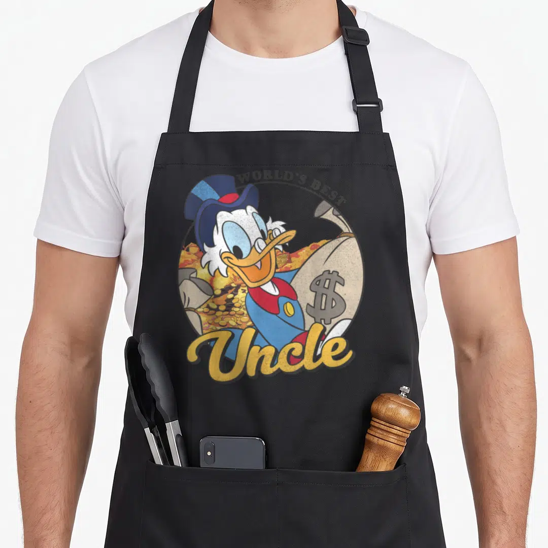 Ducktale uncle apron - Scrooge McDuck holding money bag with WORLD'S BEST and Uncle text in blue yellow gold — shown on a black cotton canvas apron against a white background