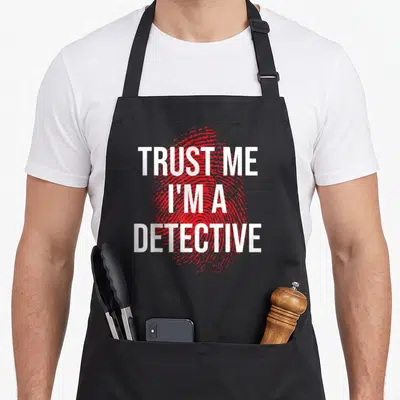 Trust detective apron - Red fingerprint graphic with white text TRUST ME I'M A DETECTIVE stacked vertically — shown on a black cotton canvas apron against a white background
