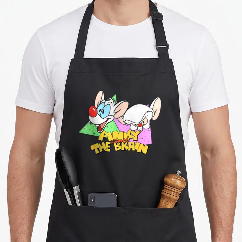 Pinky brain apron - Two cartoon mice above stacked yellow text PINKY and THE BRAIN with green and purple triangles — shown on a black cotton canvas apron against a white background