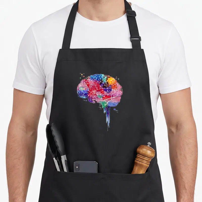 Colourful human anatomy apron - Multicolored watercolor brain with blue red yellow purple green drips and bubbles — shown on a black cotton canvas apron against a white background