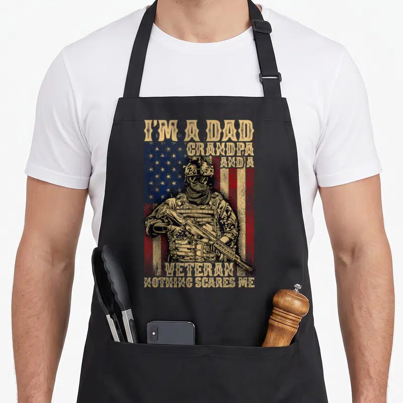 Flag grandpa 4th of july apron - Distressed soldier in front of USA flag with tan text I'm a Dad Grandpa and a Veteran — shown on a black cotton canvas apron against a white background