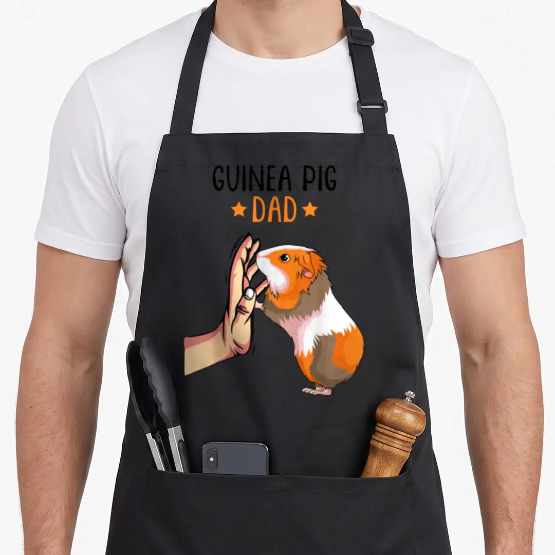 Funny guinea father day apron - Cartoon guinea pig high-fiving human hand with GUINEA PIG DAD text — shown on a black cotton canvas apron against a white background