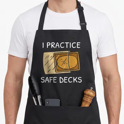 Deckss safe apron - I Practice Safe Decks text with two overlapping tan and orange playing cards — shown on a black cotton canvas apron against a white background