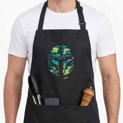 Mando tropical print aprons - Helmet silhouette filled with green teal purple and white floral pattern above white — shown on a black cotton canvas apron against a white background