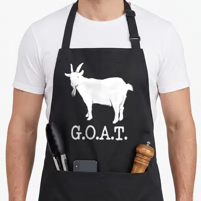 Greatest modern apron - White goat silhouette standing above G.O.A.T. text in minimalist style — shown on a black cotton canvas apron against a white background