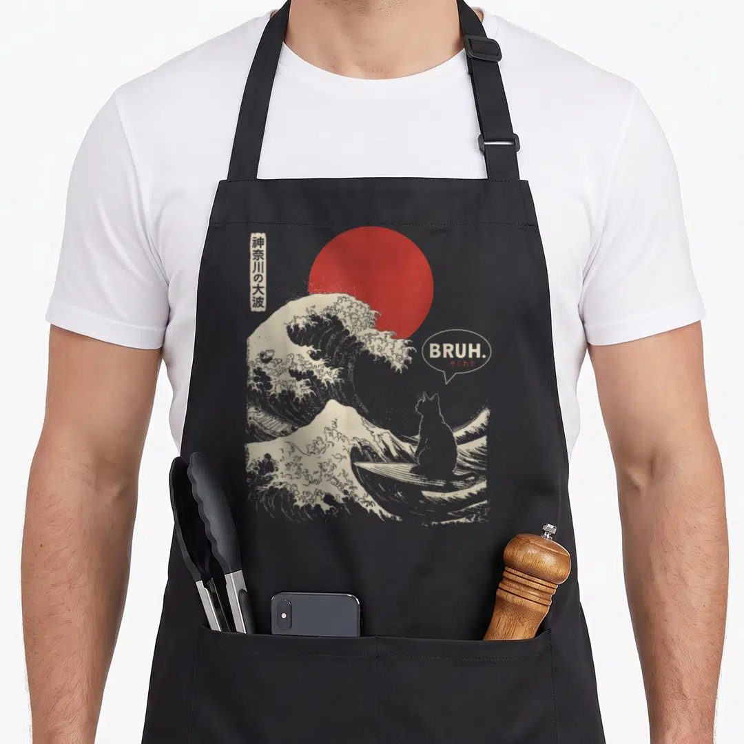 Surfing cat apron - Minimalist grey wave with red sun, cat in boat, BRUH. text, and Japanese characters — shown on a black cotton canvas apron against a white background