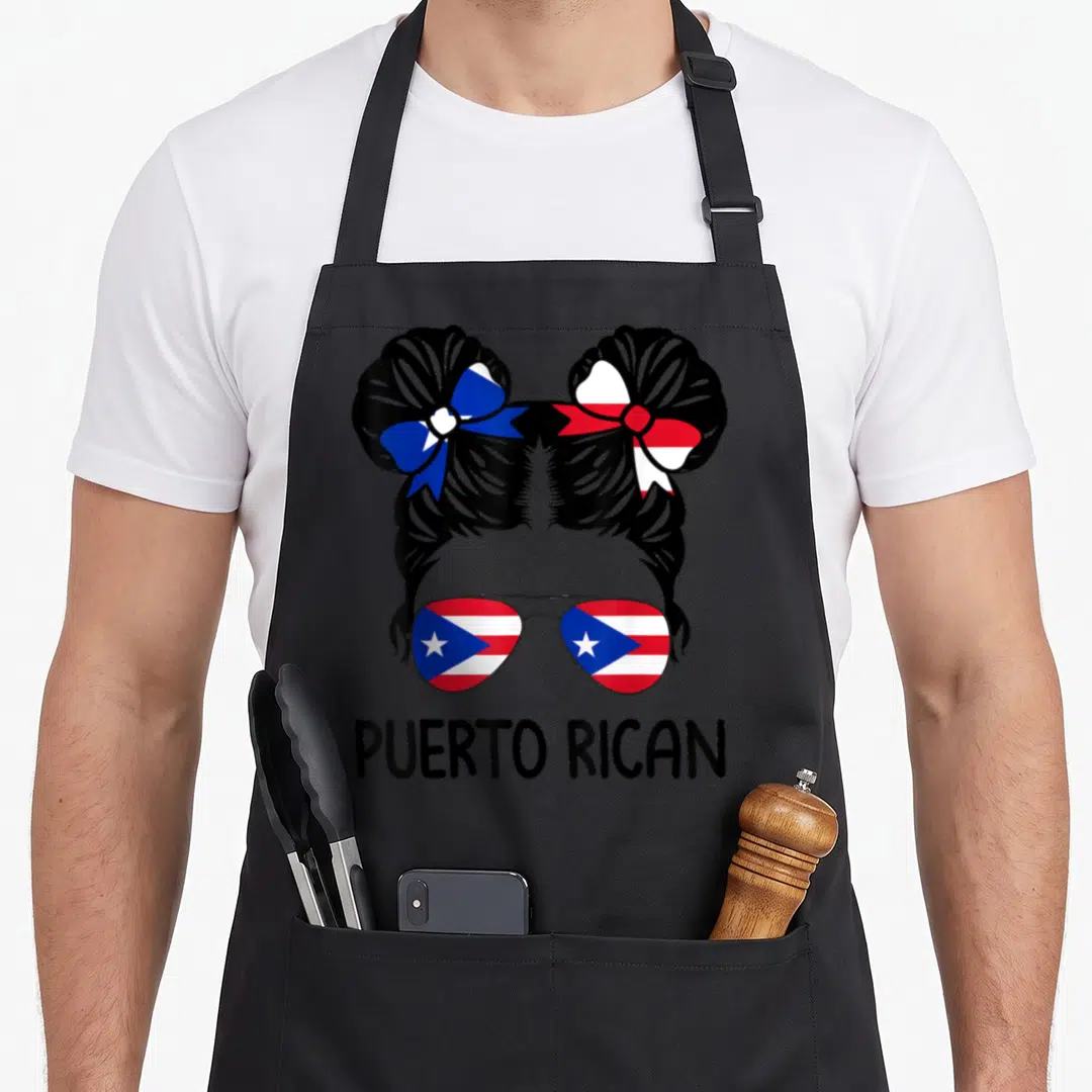 Puerto messy aprons - Woman silhouette with two buns, flag sunglasses, and PUERTO RICAN text — shown on a black cotton canvas apron against a white background