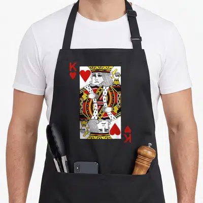 Blackjack king apron - Mirrored King of Hearts playing card in red, yellow, white, and black line art with corner K — shown on a black cotton canvas apron against a white background
