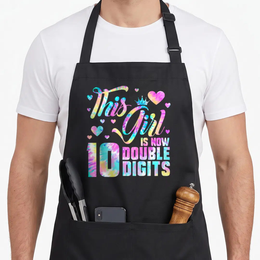 Birthday double apron - Tie-dye text This Girl Is Now Double Digits 10 with crown and hearts — shown on a black cotton canvas apron against a white background
