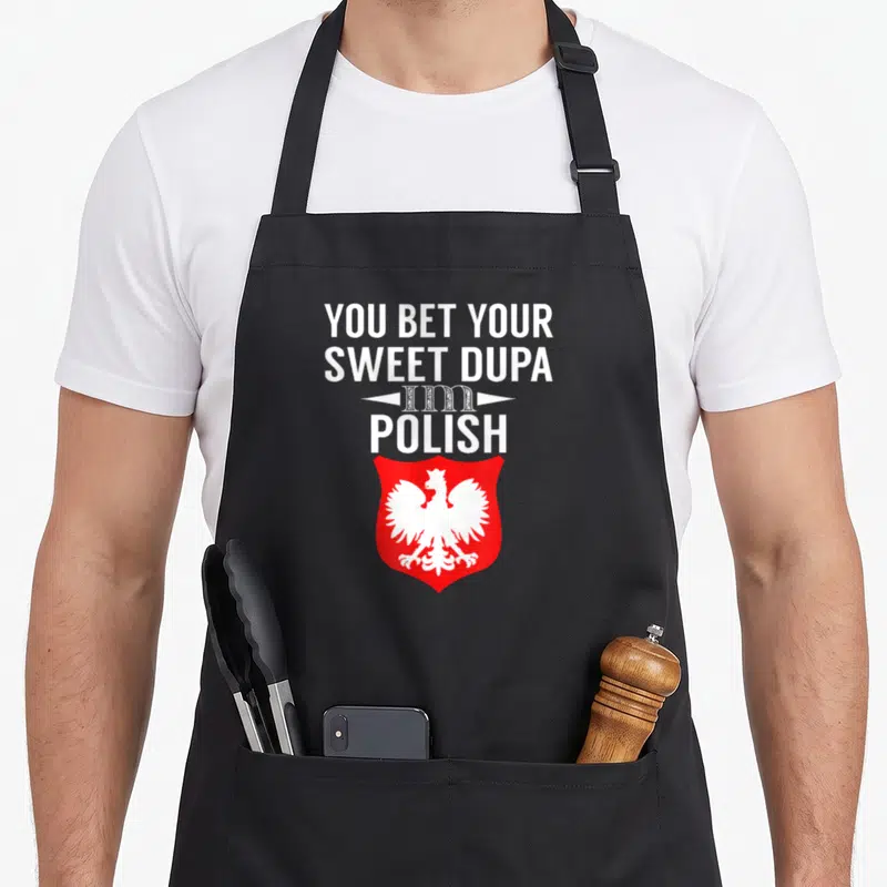Dupa polish aprons - Stacked white text above red shield containing white Polish eagle emblem — shown on a black cotton canvas apron against a white background