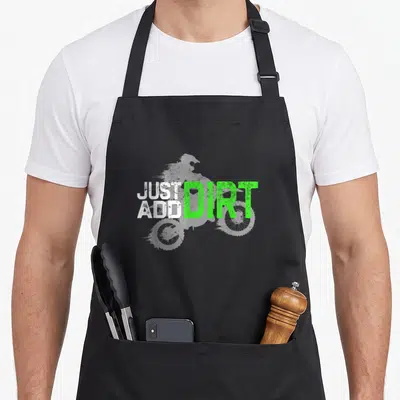 Youth bike apron - Grey dirt bike silhouette with stacked white text JUST ADD and large green text DIRT — shown on a black cotton canvas apron against a white background