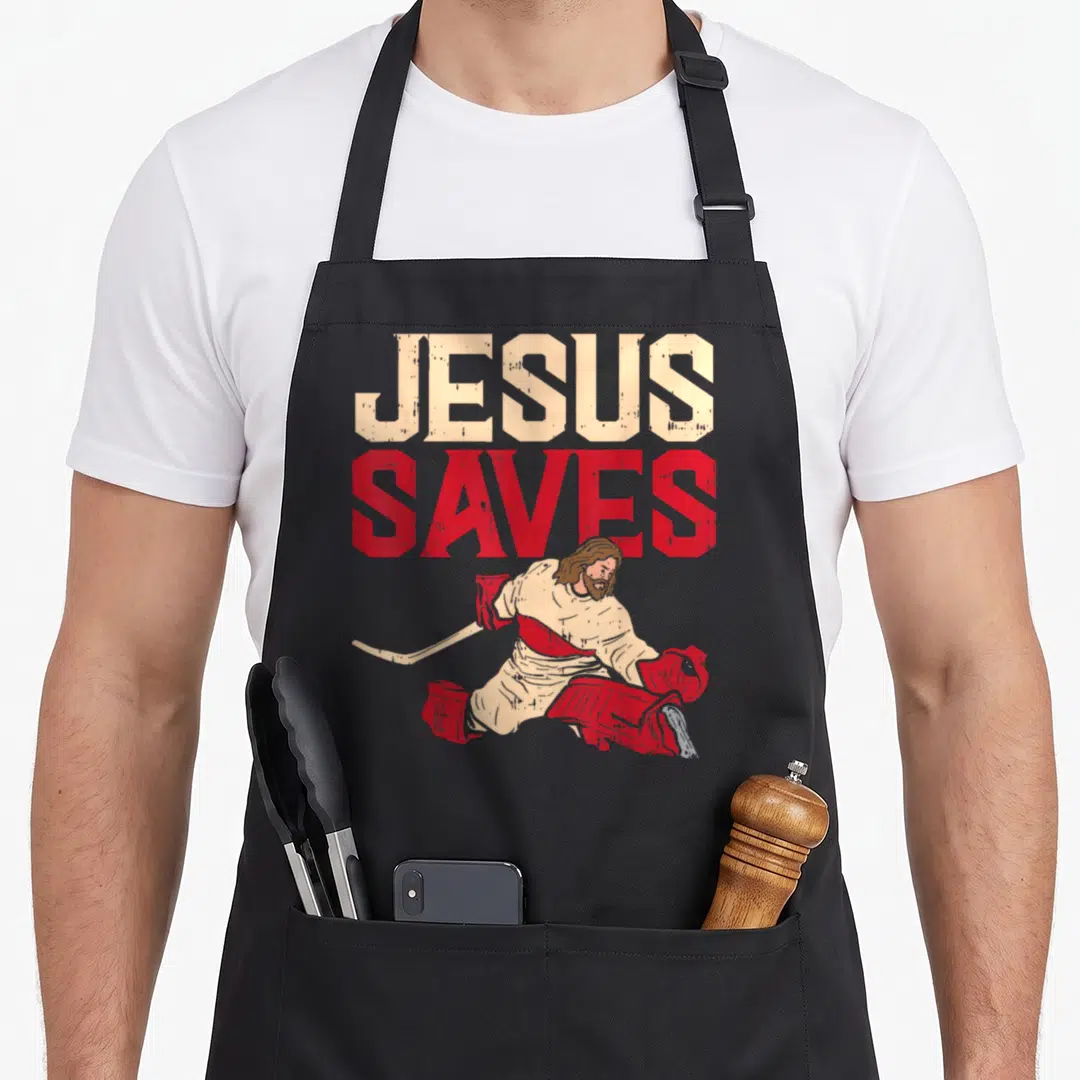 Ice christian apron - JESUS SAVES text above distressed goalie Jesus in red and cream — shown on a black cotton canvas apron against a white background