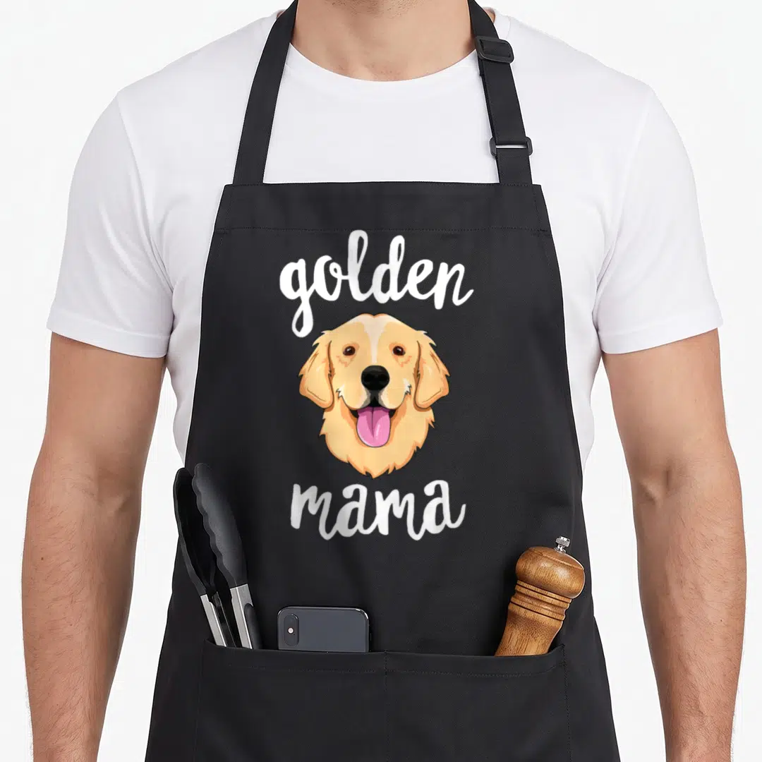Mama golden retriever apron - Cartoon golden retriever head with pink tongue between white golden and mama text — shown on a black cotton canvas apron against a white background