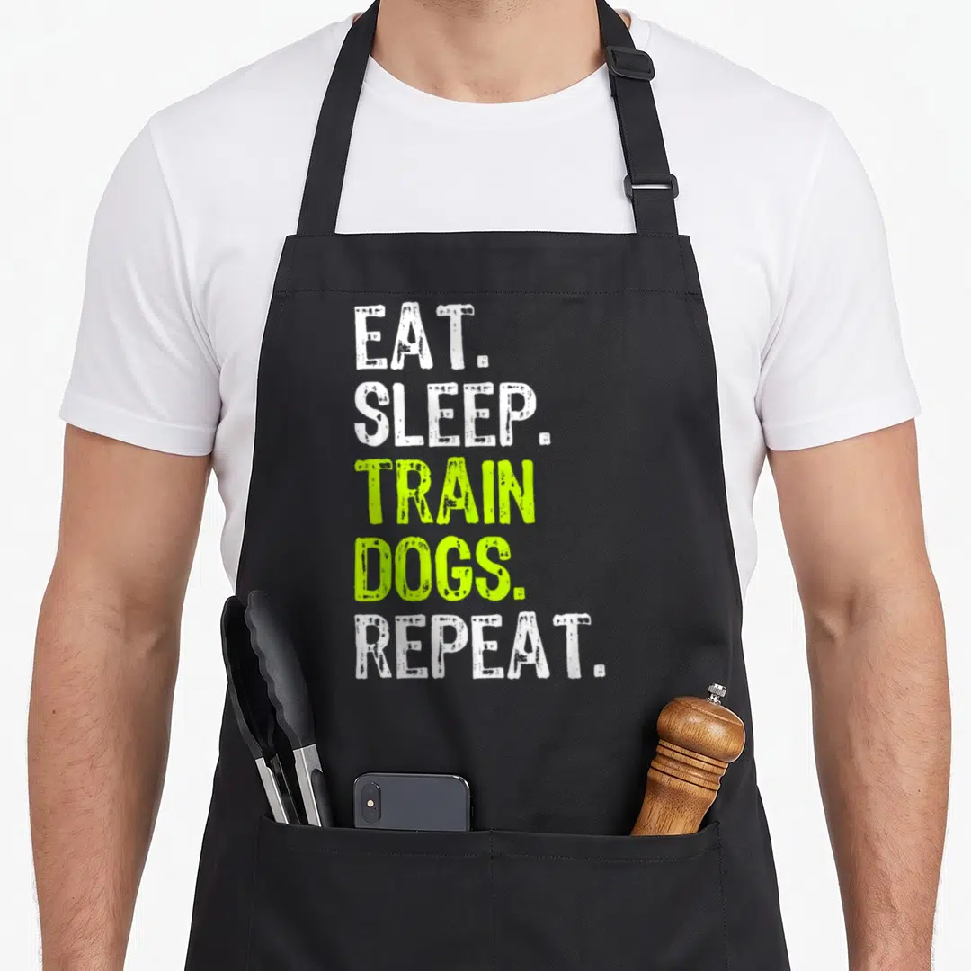 Eat dog training apron - Stacked white and lime green text reading EAT SLEEP TRAIN DOGS REPEAT — shown on a black cotton canvas apron against a white background