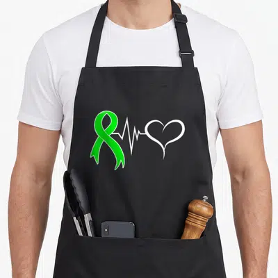 Living donor organ apron - Green awareness ribbon connected by white heartbeat line to white heart outline — shown on a black cotton canvas apron against a white background