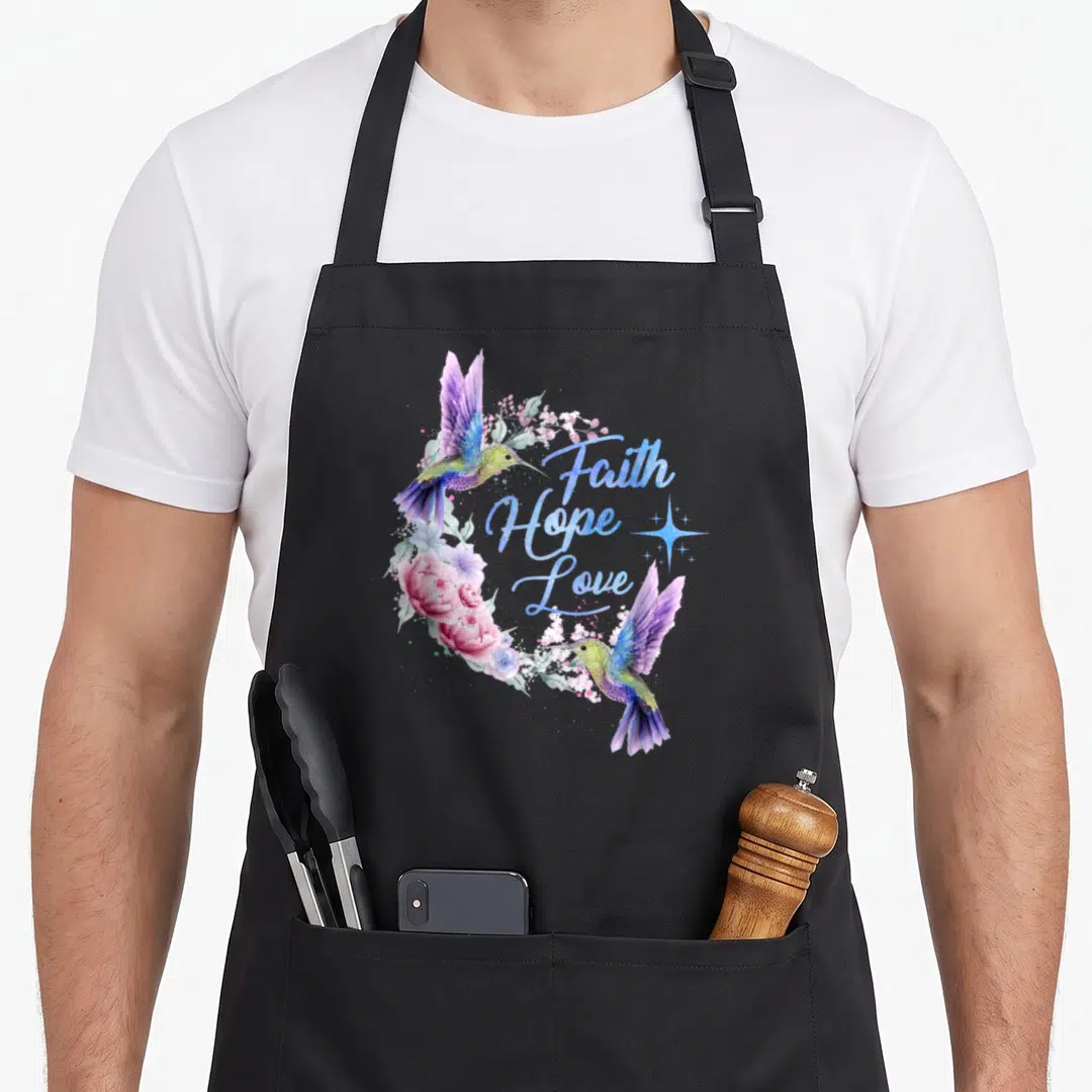 Hope bird apron - Two hummingbirds in purple blue pink and green watercolor framing Faith Hope Love text with a star — shown on a black cotton canvas apron against a white background
