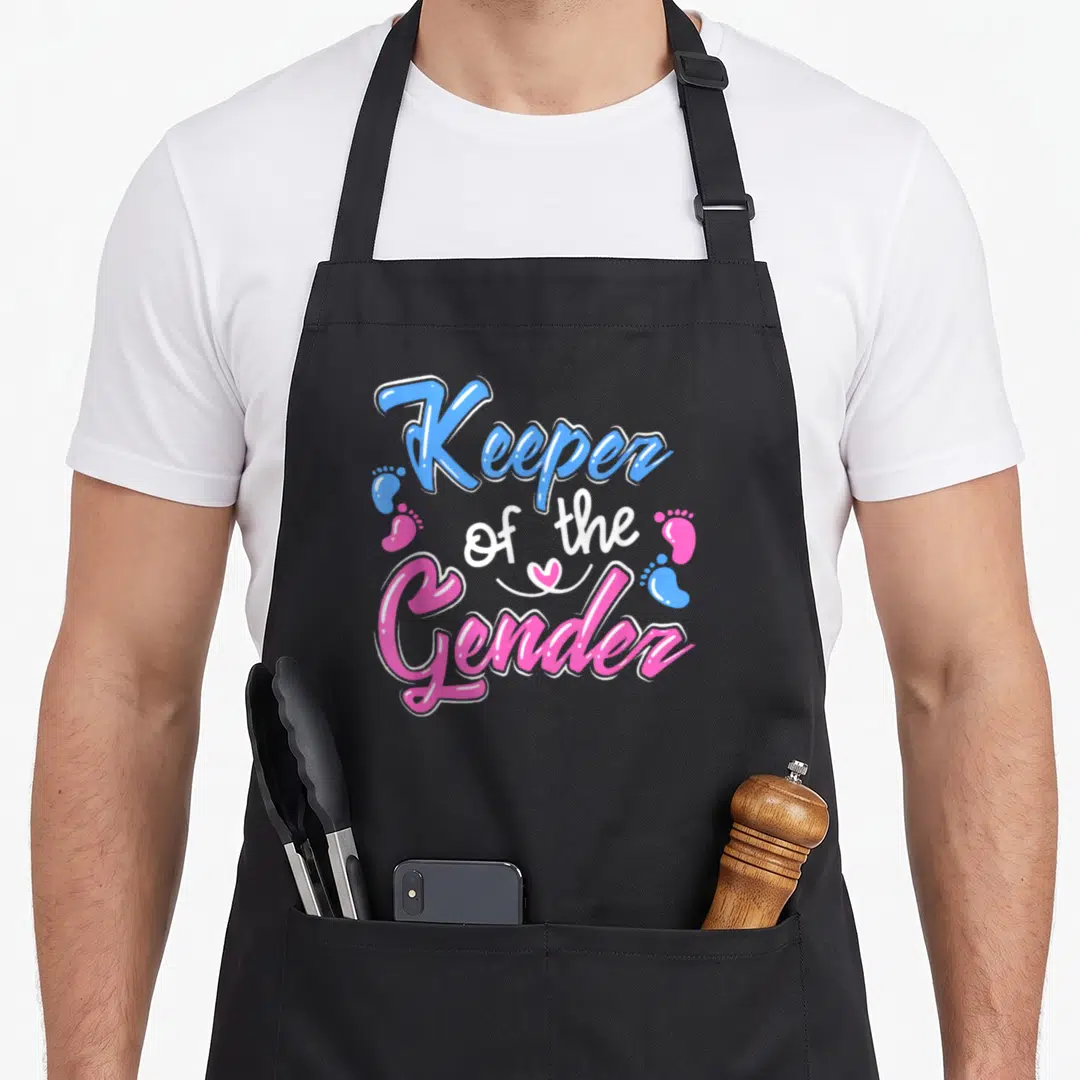 Announcement gender reveal apron - Blue pink and white text reading Keeper of the Gender with baby footprints and heart — shown on a black cotton canvas apron against a white background