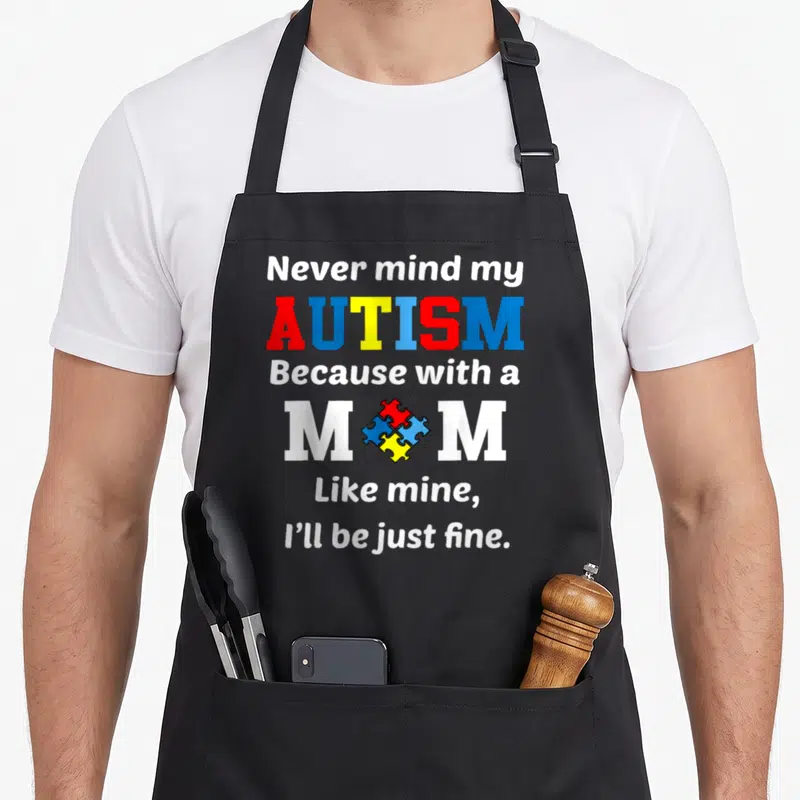 Autism awareness ribbon apron - Stacked text reading Never mind my Autism with a colorful puzzle piece replacing the O — shown on a black cotton canvas apron against a white background