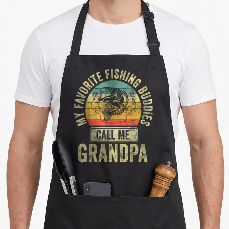 Call grandpa fishing apron - Retro fish jumping over tan teal orange red sunset bands with arched text — shown on a black cotton canvas apron against a white background