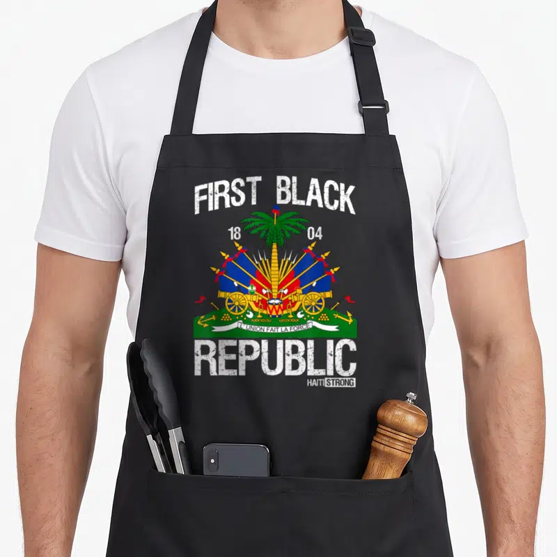 History haitian apron - First Black Republic text surrounding coat of arms with palm tree and cannons in distressed — shown on a black cotton canvas apron against a white background