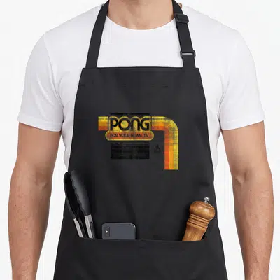 Atari gamer retro apron - Pong logo with yellow orange stripes and Atari mark on black background — shown on a black cotton canvas apron against a white background