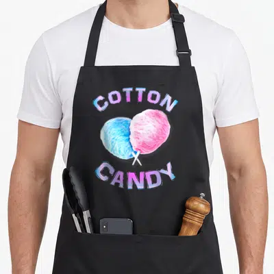 Stick candy aprons - Arched COTTON CANDY text framing crossed blue and pink cotton candy sticks in cartoon style — shown on a black cotton canvas apron against a white background