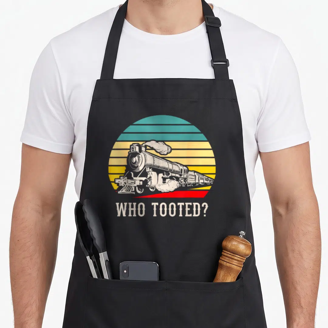 Tooted locomotive railroad apron - Retro steam train in striped circle with text WHO TOOTED below — shown on a black cotton canvas apron against a white background