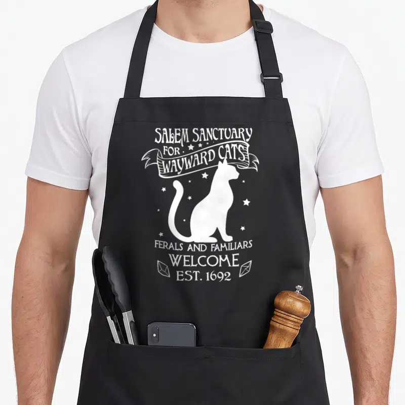 Witch cat apron - White cat silhouette with arched text reading Salem Sanctuary for Wayward Cats and Est 1692 — shown on a black cotton canvas apron against a white background