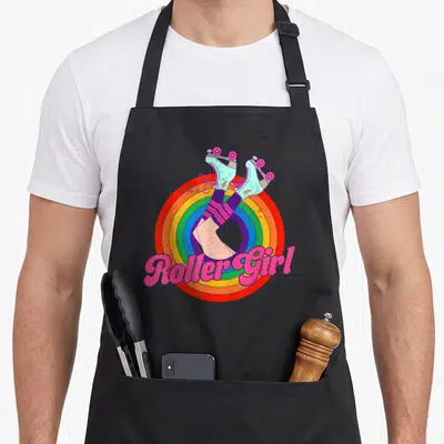 Skate 70s apron - Roller Girl text over rainbow circle with teal roller skates and striped socks — shown on a black cotton canvas apron against a white background
