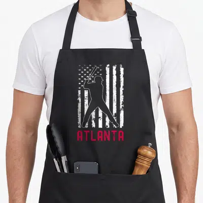 Atlanta american flag apron - White baseball batter silhouette over distressed flag with red ATLANTA text below — shown on a black cotton canvas apron against a white background