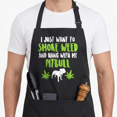 Smoke dog apron - I just want to smoke weed and hang with my pitbull text with dog and leaves — shown on a black cotton canvas apron against a white background