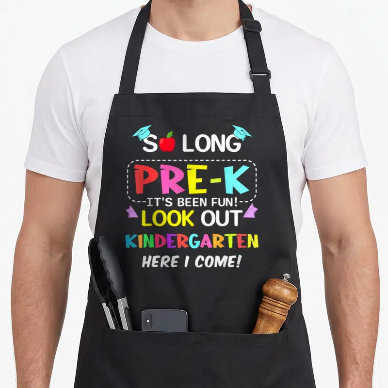 Pre come and get it apron - Stacked colorful Pre-K graduation text with apple, caps, and planes — shown on a black cotton canvas apron against a white background
