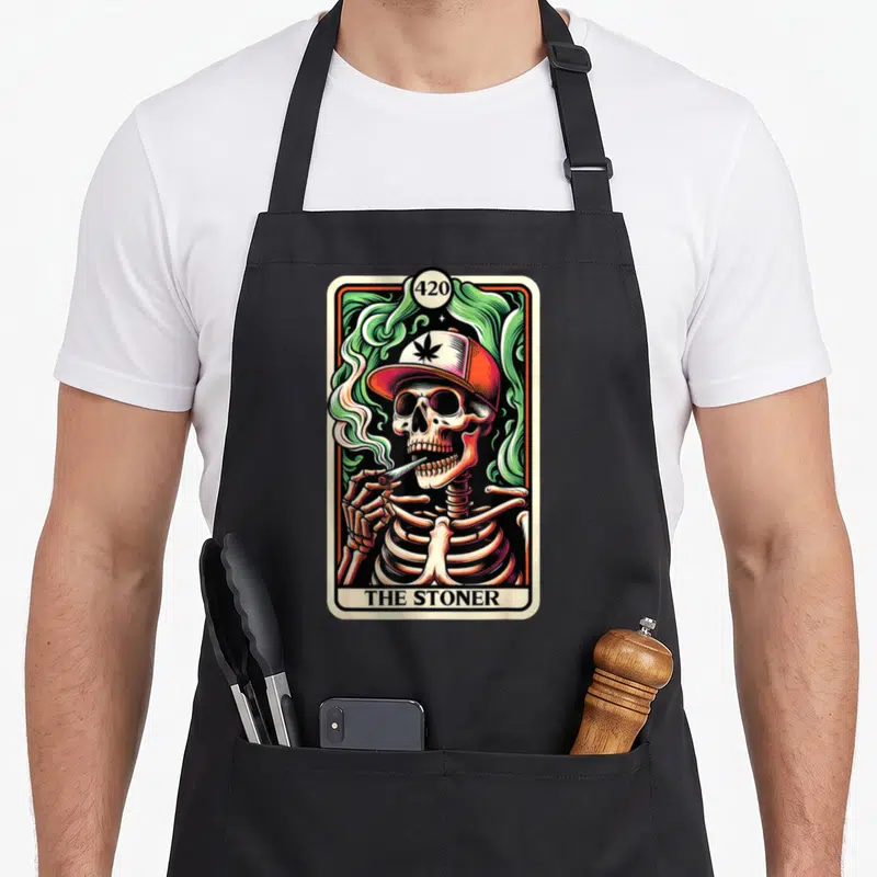 Tarot skeleton apron - Cartoon skeleton in cap smoking joint inside tarot frame with 420 and THE STONER text — shown on a black cotton canvas apron against a white background