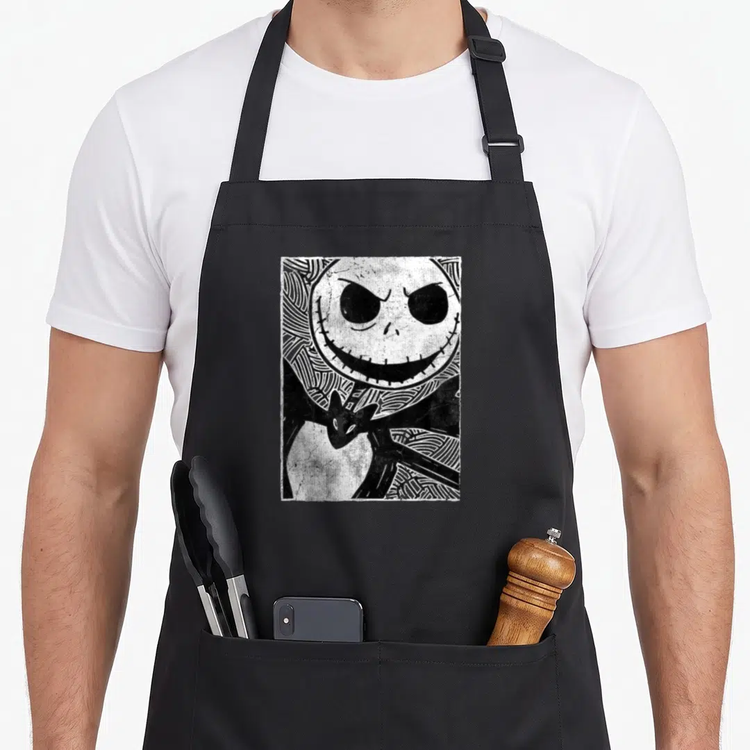Nighmare christmas apron - Black and white sketch of a stitched skull face with a bat below — shown on a black cotton canvas apron against a white background
