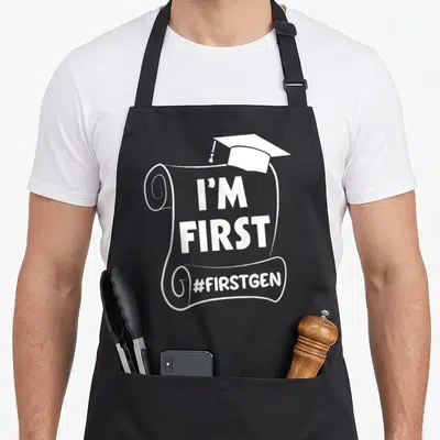 Generation student aprons - White diploma scroll with cap and I'M FIRST #FIRSTGEN text — shown on a black cotton canvas apron against a white background